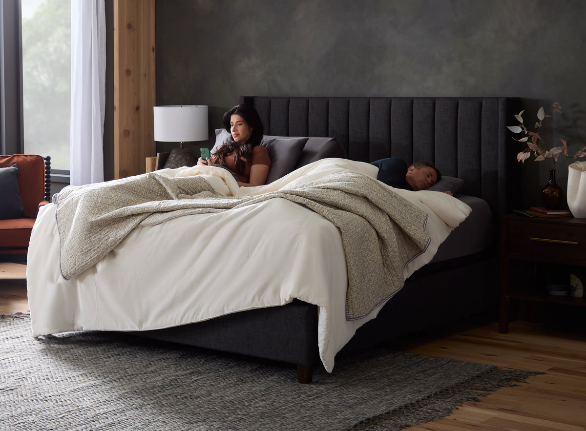 A Malouf Ice Cloud mattress on a dark upholstered bed frame in a bedroom, with two white pillows and the MALOUF wordmark visible on the mattress side.